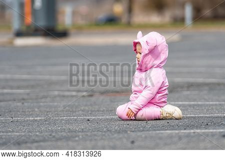 A Little Child In A Pink Dress Crawling On The Asphalt In A Car Parking Lot