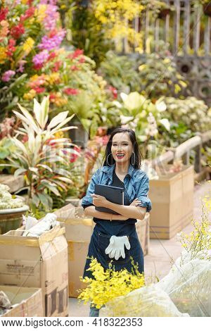 Portrait Of Happy Joyful Young Vietnamese Woman With Tablet Computer Standing In Greenhouse Full Of 