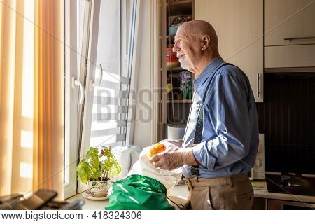 Senior man in kitchen at home looking out of window
