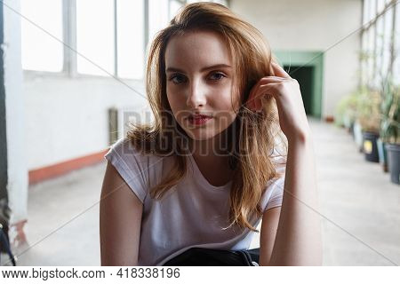 Young Caucasian Girl Sits In T-shirt At Coridor With Windows And Houseplants