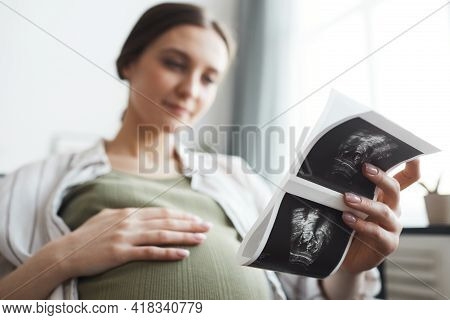 Pregnant Woman Holding X-ray Image Of Her Baby During Her Rest On The Sofa At Home