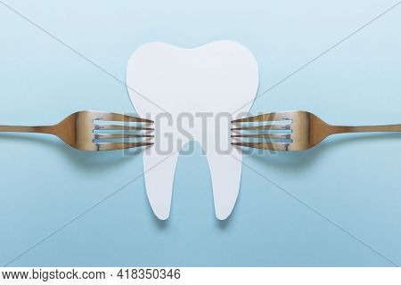 One Large Paper Tooth With Two Metallic Silver Forks On Blue Background.