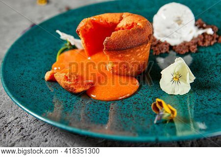 Carrot Fondant Cake with Ice Cream. Carrot Cake with liquid center served hot with ice cream. Dark green restaurant dish on textured gray table