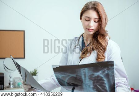 Female American Doctor Of Asian Descent Is Analyzing An X-ray Image Of An Office Patient.