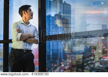 Businessman Standing At Window Of Office Building Overlooking At Cityscpae