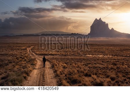 Woman Walking On A Dirt Road In The Dry Desert With A Mountain Peak In The Background. Dramatic Suns