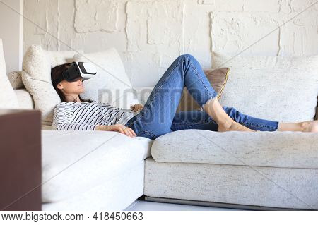 Young Casual Girl Wearing Vr Headset While Lounging On Couch At Home And Looking Around.