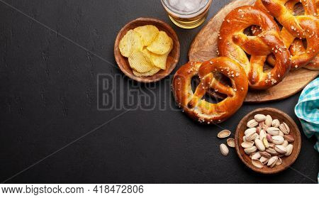 Lager beer mug, nuts, potato chips and fresh baked homemade pretzel with sea salt on stone table. Classic beer snack. Top view flat lay with copy space