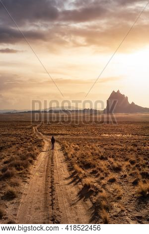 Woman Walking On A Dirt Road In The Dry Desert With A Mountain Peak In The Background. Dramatic Suns