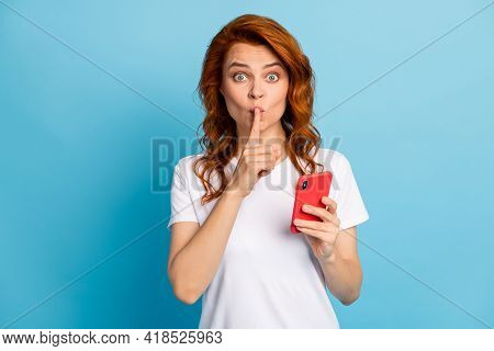 Photo Portrait Of Girl Covering Mouth With Finger Holding Phone In One Hand Isolated On Pastel Blue 