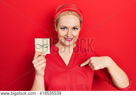 Young blonde woman holding infinite symbol reminder pointing finger to one self smiling happy and proud 