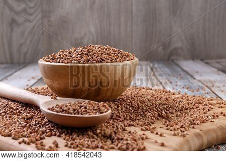 Scattered Buckwheat. Buckwheat In A Wooden Bowl And Spoon Lies On A Wooden Table. Scattered Buckwhea