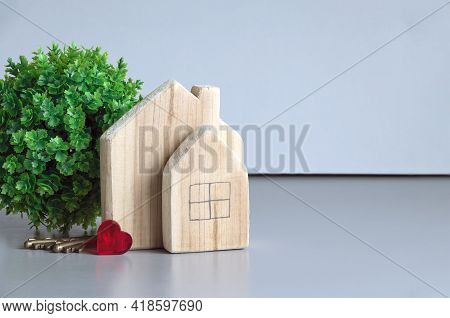 A Green Plant, Wooden Houses, Keys And A Red Heart On A Gray Background. The Concept Of Love In The 