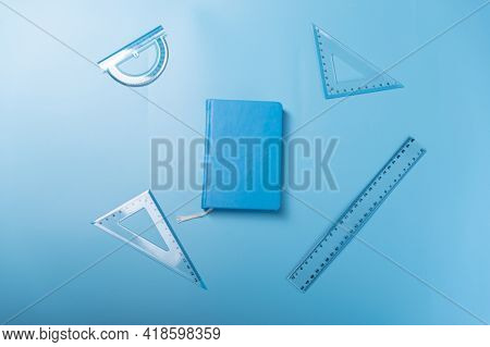 A Variety Of Rulers And A Notebook. Blue Rulers And Blue Notepad On A Blue Background. Top.