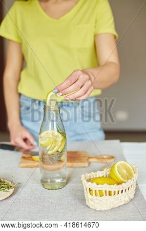 Female Hand Put Lemon In Glass Bottle, Making Detox Healthy Water With Lemon And Rosemary