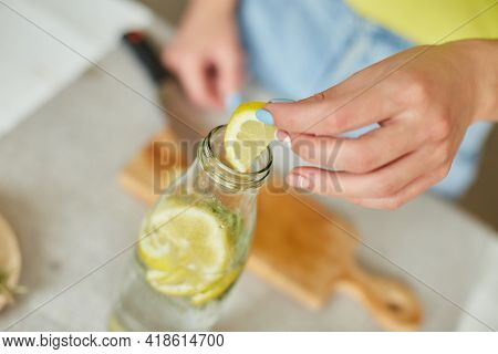 Female Hand Put Lemon In Glass Bottle, Making Detox Healthy Water With Lemon And Rosemary