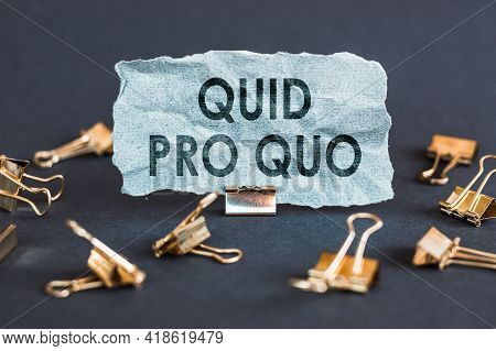 A Scrap Of Blue Paper With Clips On A Gray Background With The Text Quid Pro Quo.