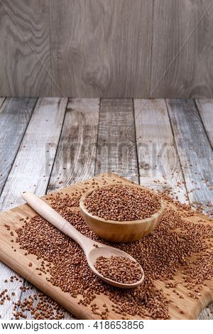 Scattered Buckwheat. Buckwheat In A Wooden Bowl And Spoon Lies On A Wooden Table. Scattered Buckwhea