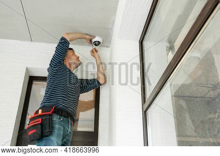 Man Stands On Stepladder And Installs Security Camera In A Private House Under Construction.