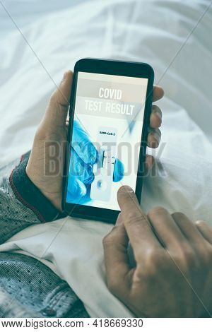 a young caucasian man wearing pajamas, lying in bed, checking the result of his covid test in a simulated app in his smartphone, that shows a negative result and reads covid test result