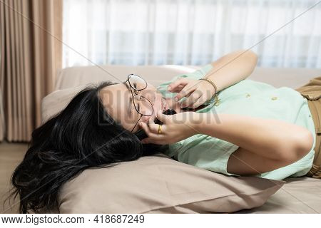 Beautiful Glasses Asian Woman Lie On Her Back And Talking Mobile In Her Bedroom With A Pastel Green 