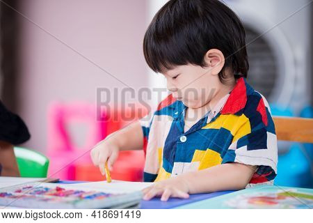 2-3 Years Old Asian Boy Is Coloring With Chalk Color On Paper Placed. Cute Baby Do Handicrafts, Make