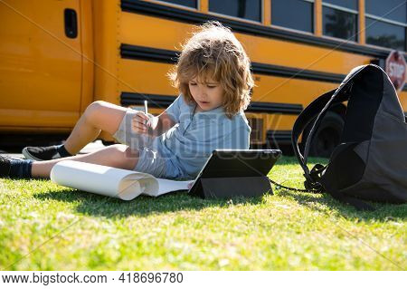 Schoolboy Writing Outdoor In School Park And Doing Homework On School Bus.