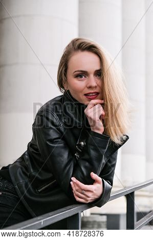 Portrait Of Young Blonde Woman With Red Lips Wearing Leather Jacket On Corporate Building Stairs. Ca