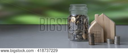 Banner For A Website About Proper Family Budget Planning. Stacks Of Coins, Wooden Houses, A Glass Ja