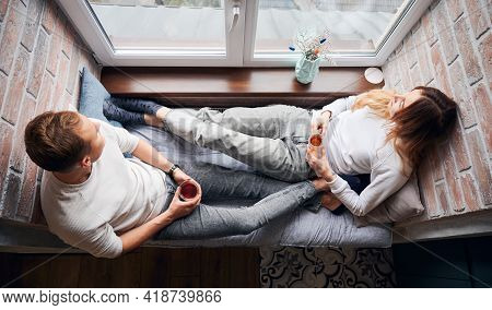 Top View Of Couple In Love Who Spending Time Together, Looking Out The Window, Drinking Warm Tea And