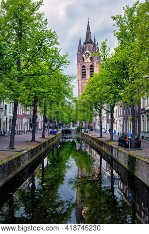 Delt canal with old houses bicycles and cars parked along and Oude Kerk Old church tower. Delft, Netherlands