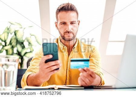 Shot Of Confident Man Holding His Credit Card And Mobile Phonem In His Hand While Doing Online Banki