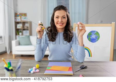distant education, school and people concept - happy smiling female teacher with color paper, glue and pompom having online class of arts and crafts at home