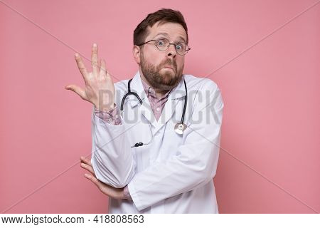 Young Caucasian Doctor Makes A Hand Gesture In Bewilderment And Looks In Surprise. Pink Background.