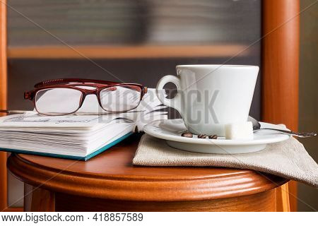 A Cup Of Coffee, A Volume Of Poetry, Women`s Reading Glasses On A Wooden Console At Home.
