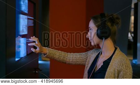 Woman Touching Interactive Display, Using Headphones And Listening Audio Guide At Modern Jewish Hist