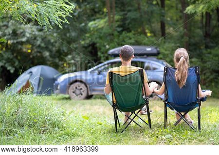 Back View Of A Happy Couple Sitting On Chairs At Campsite Relaxing Together. Travel, Camping And Vac