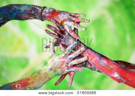 Interlacing female and male hands in the paint of different colors