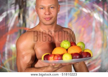 Muscular bald man with a naked torso with a plate of fruit in hand