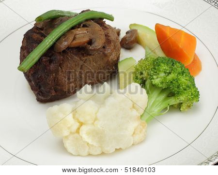 Beef tournedos (tenderloin fillet steak) served with mushrooms, steamed beans, courgettes, cauliflower, carrot and broccoli, a minimalist modern take on a traditional favourite.