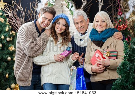 Portrait of happy family with Christmas presents and shopping bags standing in store