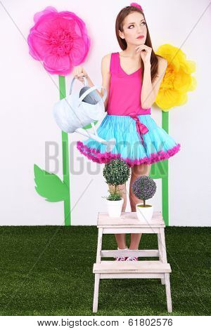 Beautiful young woman in petty skirt watering flower on decorative background