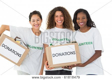 Happy team of volunteers smiling at camera holding donations boxes on white background