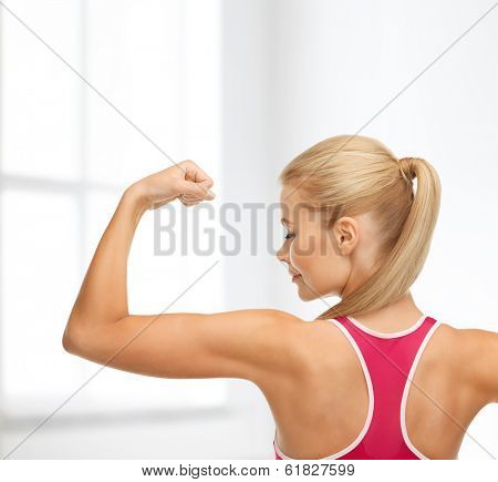 fitness and home concept - young sporty woman showing her biceps
