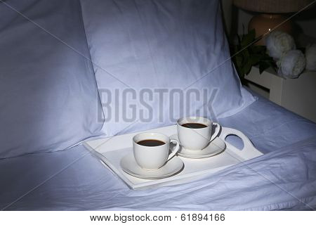 Cups of coffee on comfortable soft bed with pillows