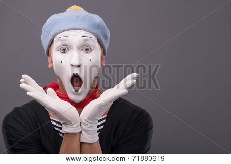 Portrait of male mime with grey hat and white face grimacing wit