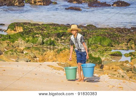 OUALIDIA, MOROCCO, APRIL 6, 2015: Boy-fisherman carries buckets with freshly caught seafood