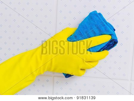 the tiles of a bathroom is cleaned with latex gloves.