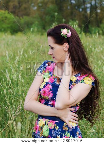 Beautiful thoughtful woman standing in a forest clearing among the tall grass on a summer evening