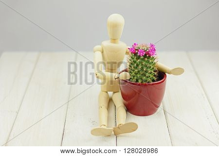 Blooming cactus in a flower pot and a mannequin on a wooden table.